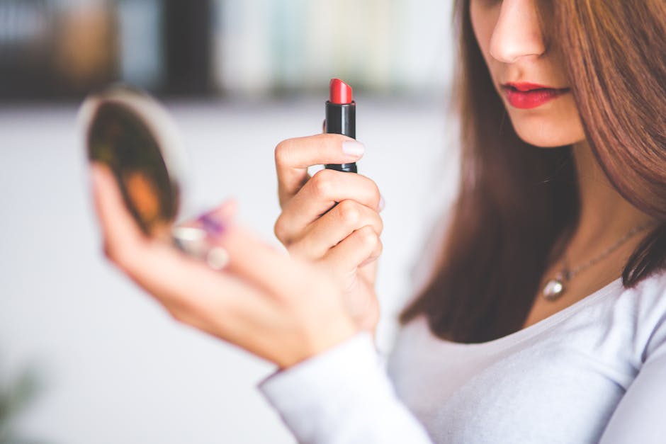 Close-up of woman applying red lipstick while holding a compact mirror