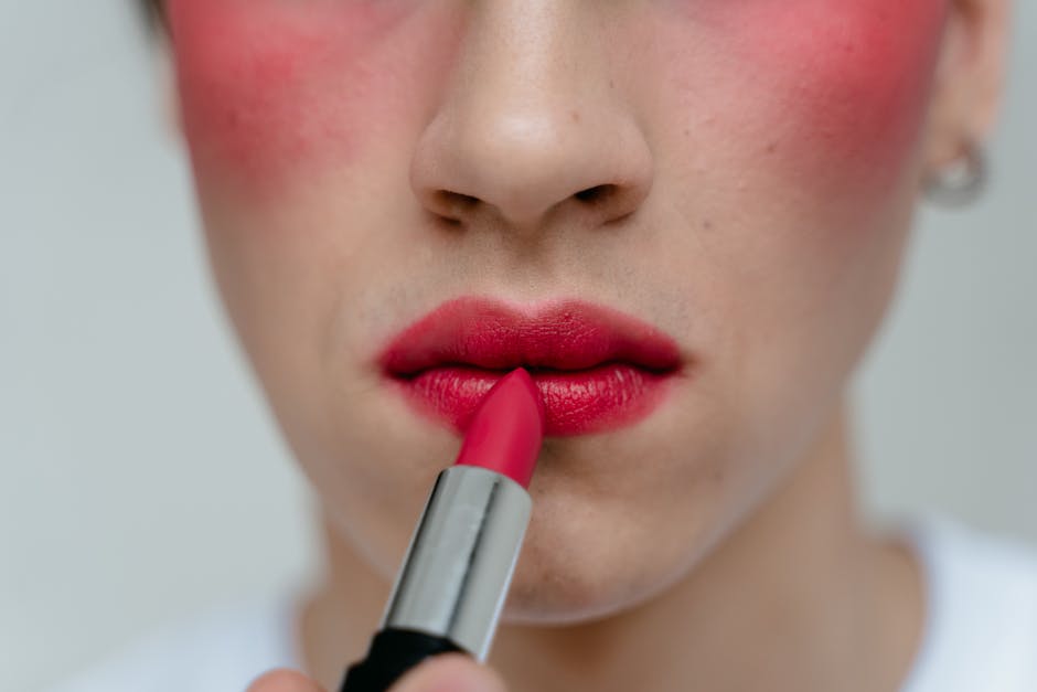 Close-up view of a person applying red lipstick to their lips, highlighting vibrant makeup
