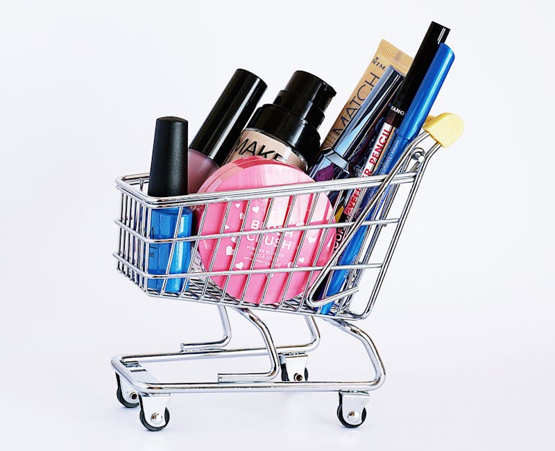Miniature shopping cart filled with a variety of cosmetics on a white background