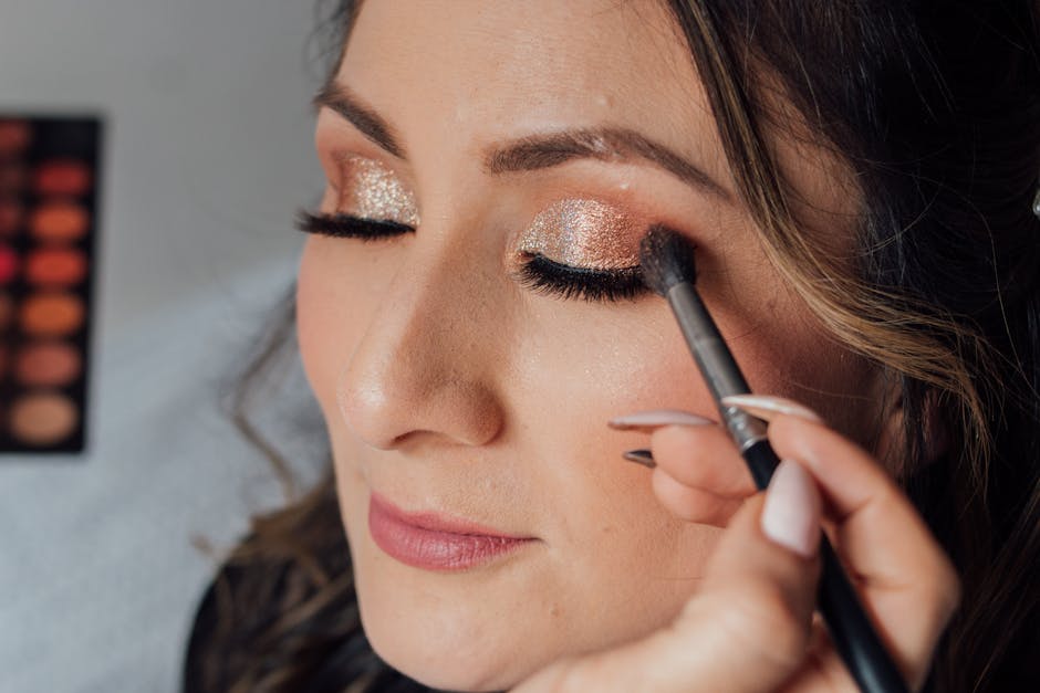 Woman receiving glamorous makeup with glitter eyeshadow and long lashes